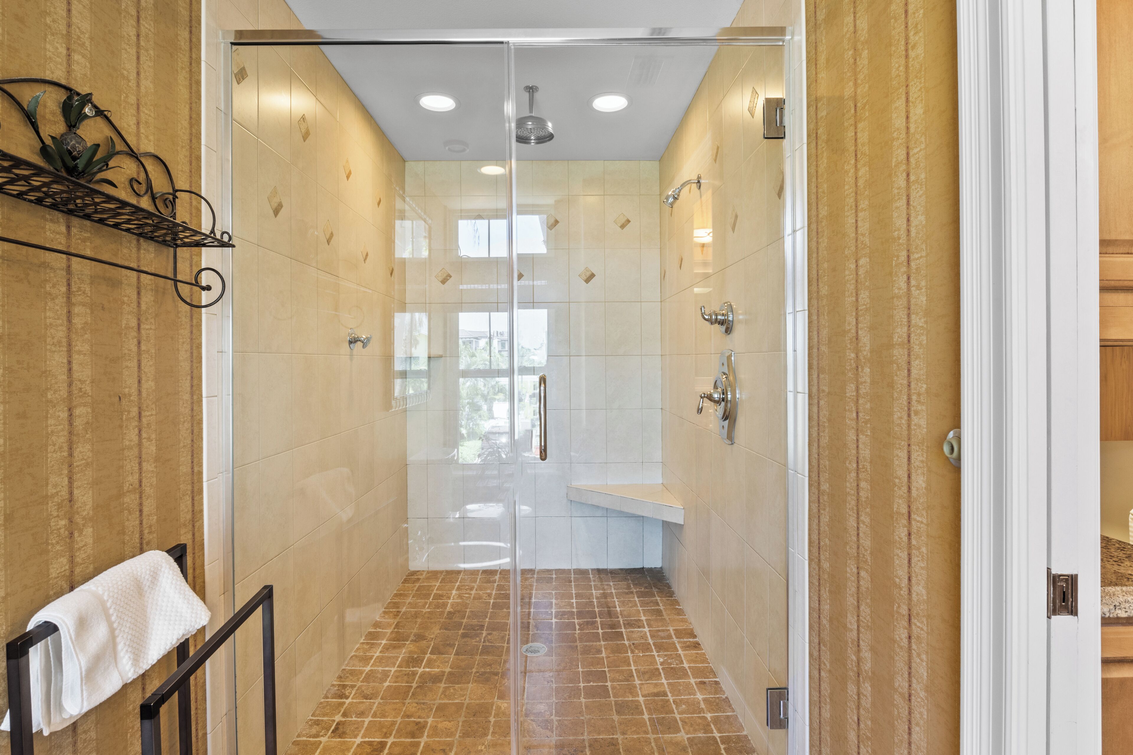 A walk-in shower with a glass door, tiled walls, and a bench.