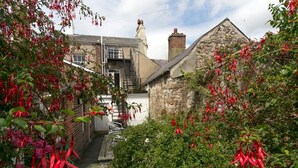A narrow alleyway with a stone building on the right and a metal staircase leading up to a door.