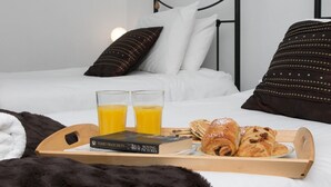 A neatly made bed with white and dark pillows, a tray with croissants and juice, and a book titled "Moving Pictures" on a wooden tray.