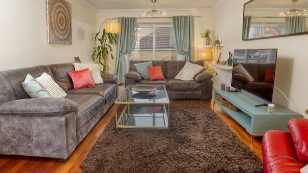 A living room with two grey sofas, a glass coffee table, a red sofa, a TV, and a large mirror.