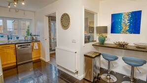 A modern kitchen with wooden cabinets, stainless steel appliances, and a black tiled floor. There are two blue bar stools and a blue abstract painting on the wall.