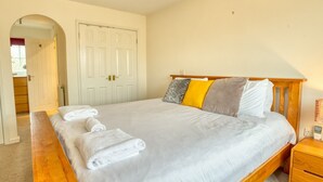 A bedroom with a large bed, a wooden headboard, a nightstand, and a white door.