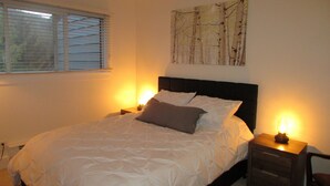 A bedroom with a bed, two bedside tables with lamps, a window with blinds, and a wall-mounted painting. - Renovated Condo, Avon Colorado, River Views and walk to Beaver Creek Shuttle (Avon)