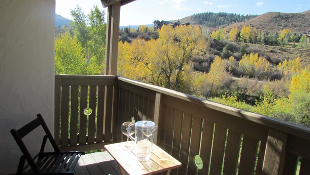A wooden deck with a table and chairs, overlooking a scenic view of autumn-colored trees and hills. - Renovated Condo, Avon Colorado, River Views and walk to Beaver Creek Shuttle (Avon)