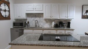 A kitchen with white cabinets, a granite countertop, a microwave, a coffee maker, and a clock. - Renovated Condo, Avon Colorado, River Views and walk to Beaver Creek Shuttle (Avon)