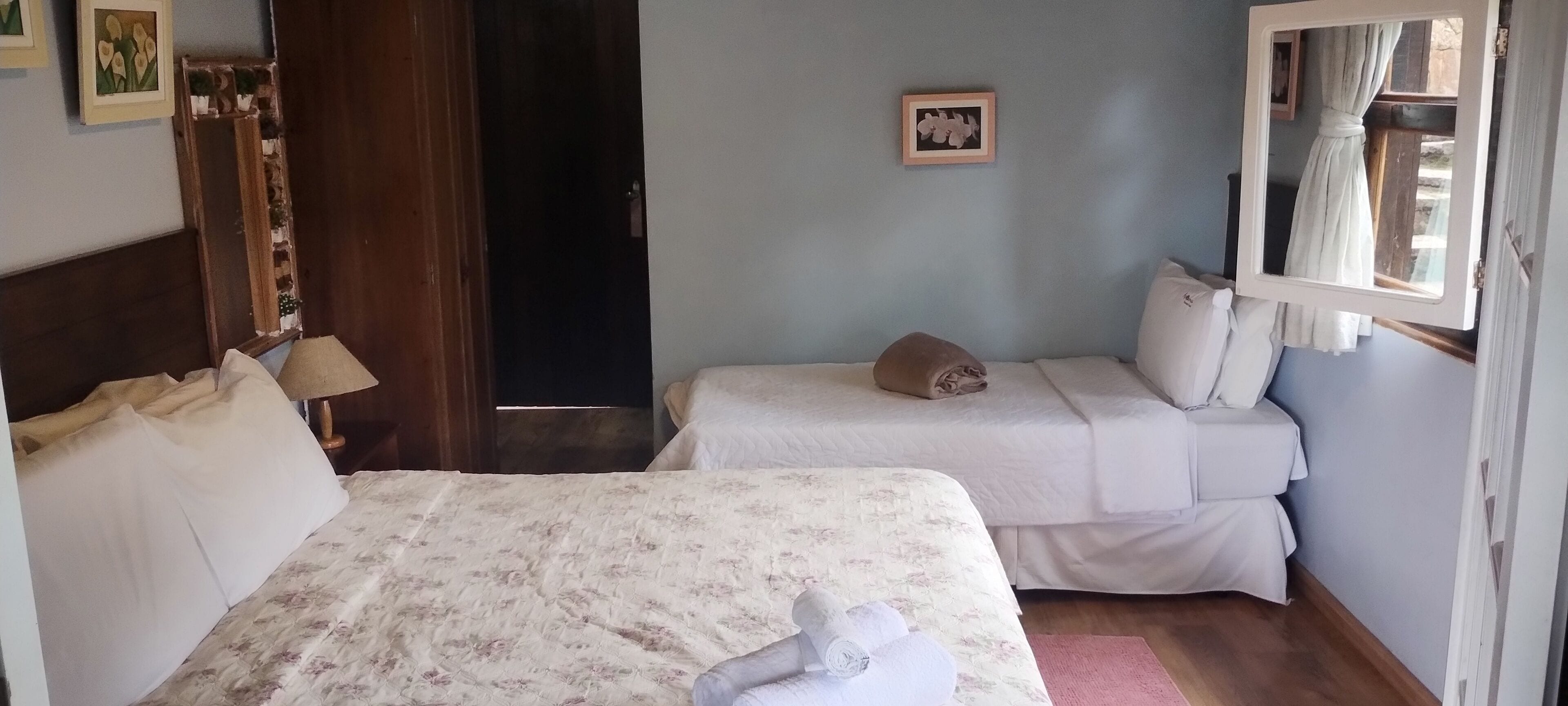 A hotel room with two beds, a wooden headboard, a mirror, and a window with curtains.