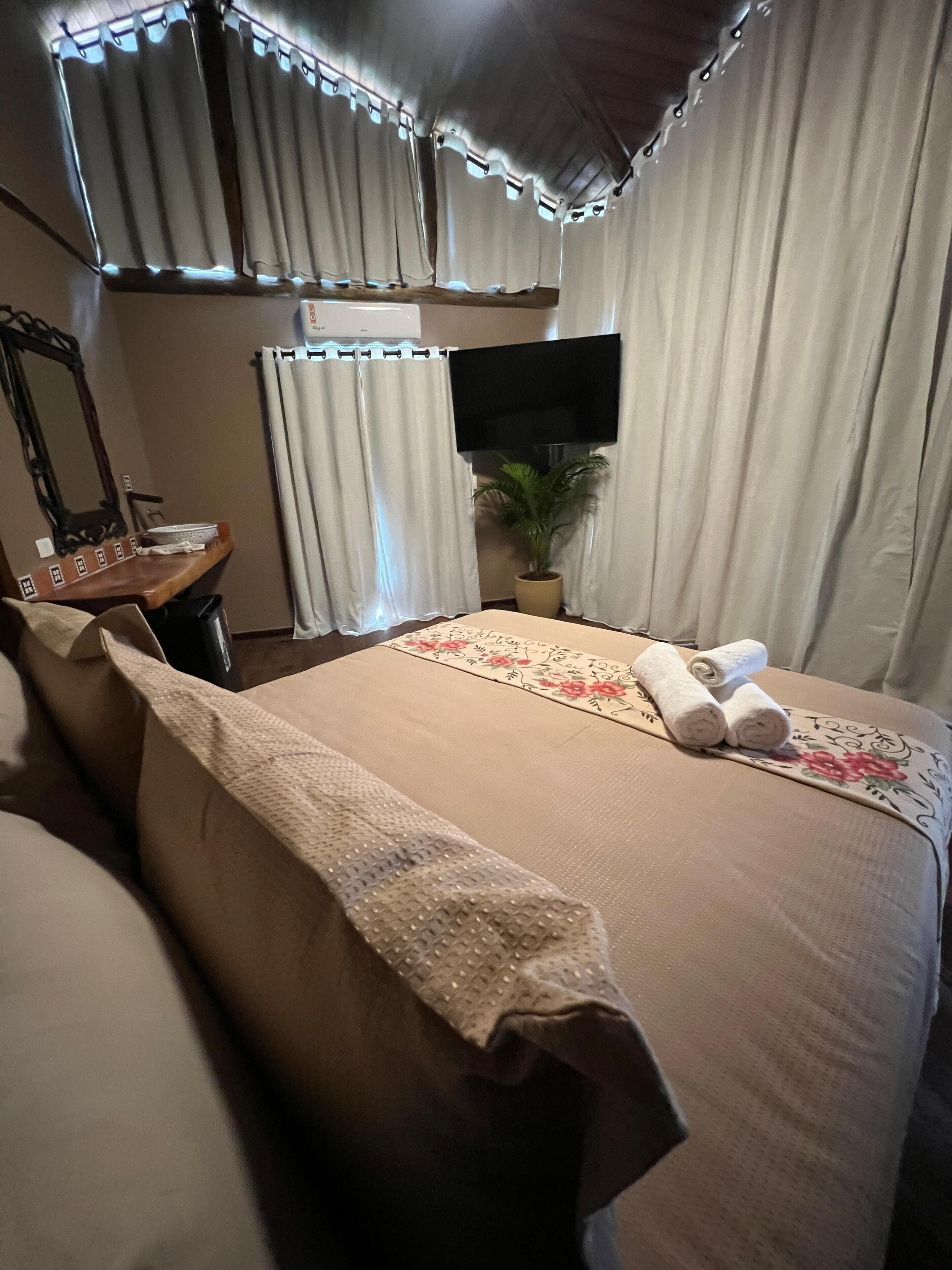 A hotel room with a bed, a TV mounted on the wall, a potted plant, and a desk with a mirror.
