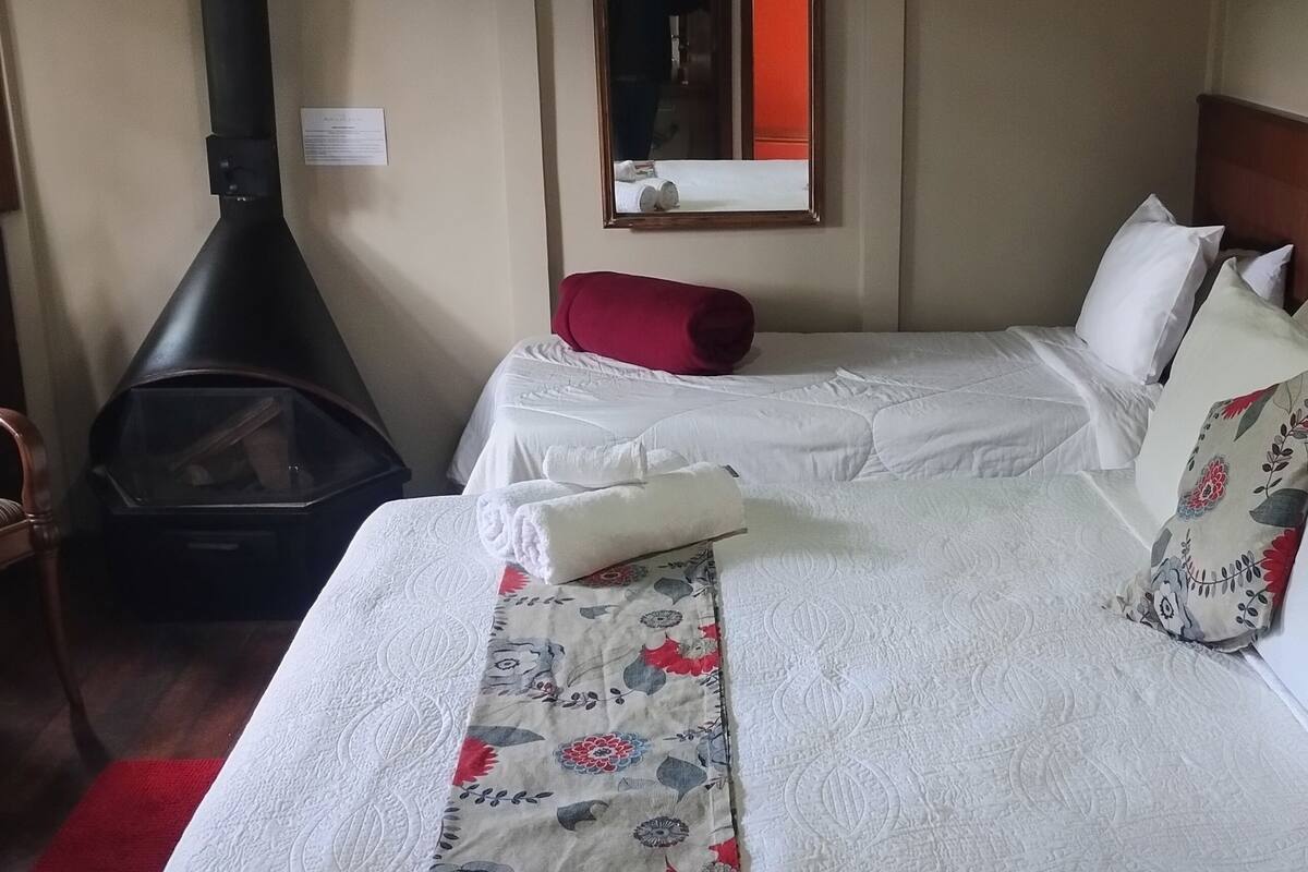 A hotel room with two beds, a wood-burning stove, a mirror, and a chair.