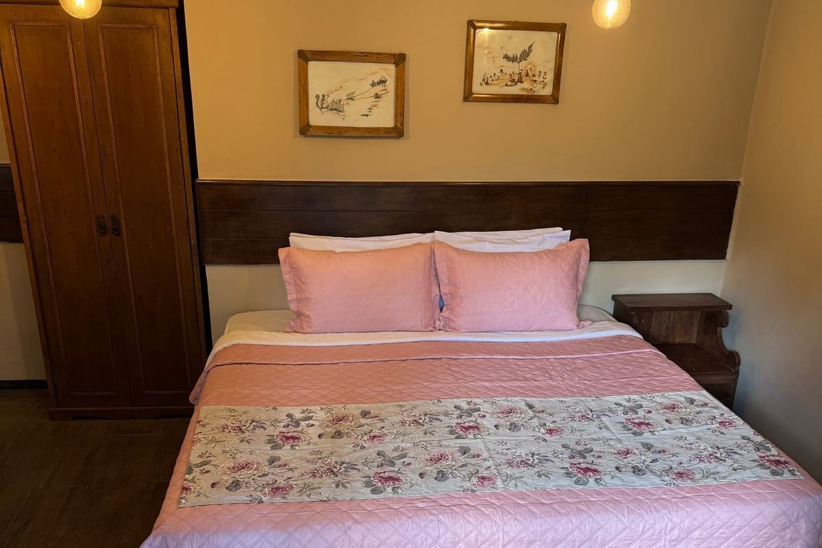 A bedroom with a bed, two wall-mounted light fixtures, a wooden wardrobe, and two framed pictures on the wall.