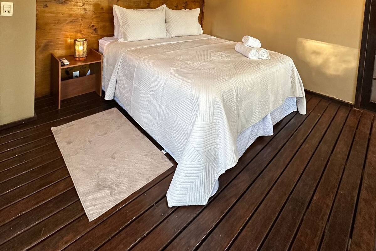 A bedroom with a wooden headboard, a bed with white bedding, a nightstand with a lamp, and a wall-mounted light fixture.
