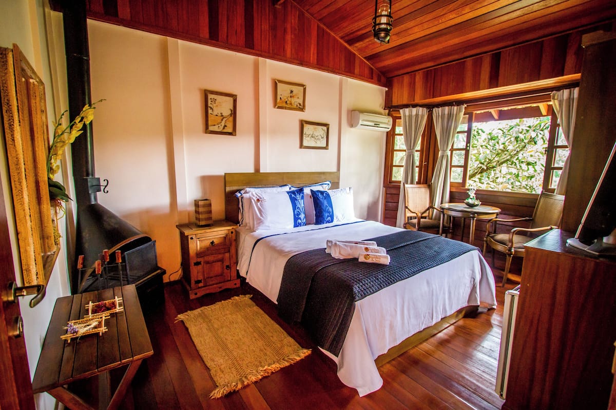 A wooden-floored bedroom with a bed, bedside tables, a desk, and a window with curtains.