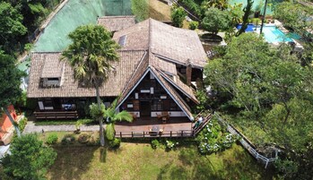 Une maison traditionnelle avec un toit à forte pente, entourée d’une végétation luxuriante et dotée d’une piscine.