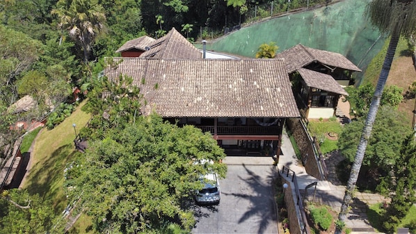 A large, two-story building with a tiled roof, surrounded by lush greenery and a swimming pool.