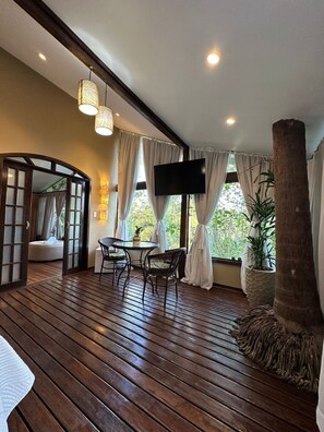 A wooden deck with a round table and chairs, a TV mounted on the wall, and a large tree trunk decoration. - Pousada Apoema (Petrópolis)