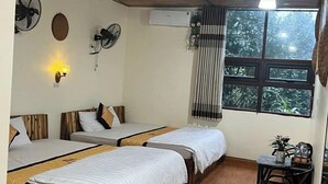 Una habitación con tres camas de madera, una mesita con una planta y una ventana con vistas al verdor.