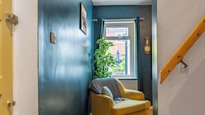 A narrow hallway with a yellow armchair, a window with a view of a building, and a clock on the wall.