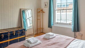 A bedroom with a bed, a dresser, a window with curtains, a radiator, and a hanging coat rack.