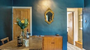 A dining area with a wooden table, chairs, a vase with flowers, a wine bottle, and a mirror on the wall.
