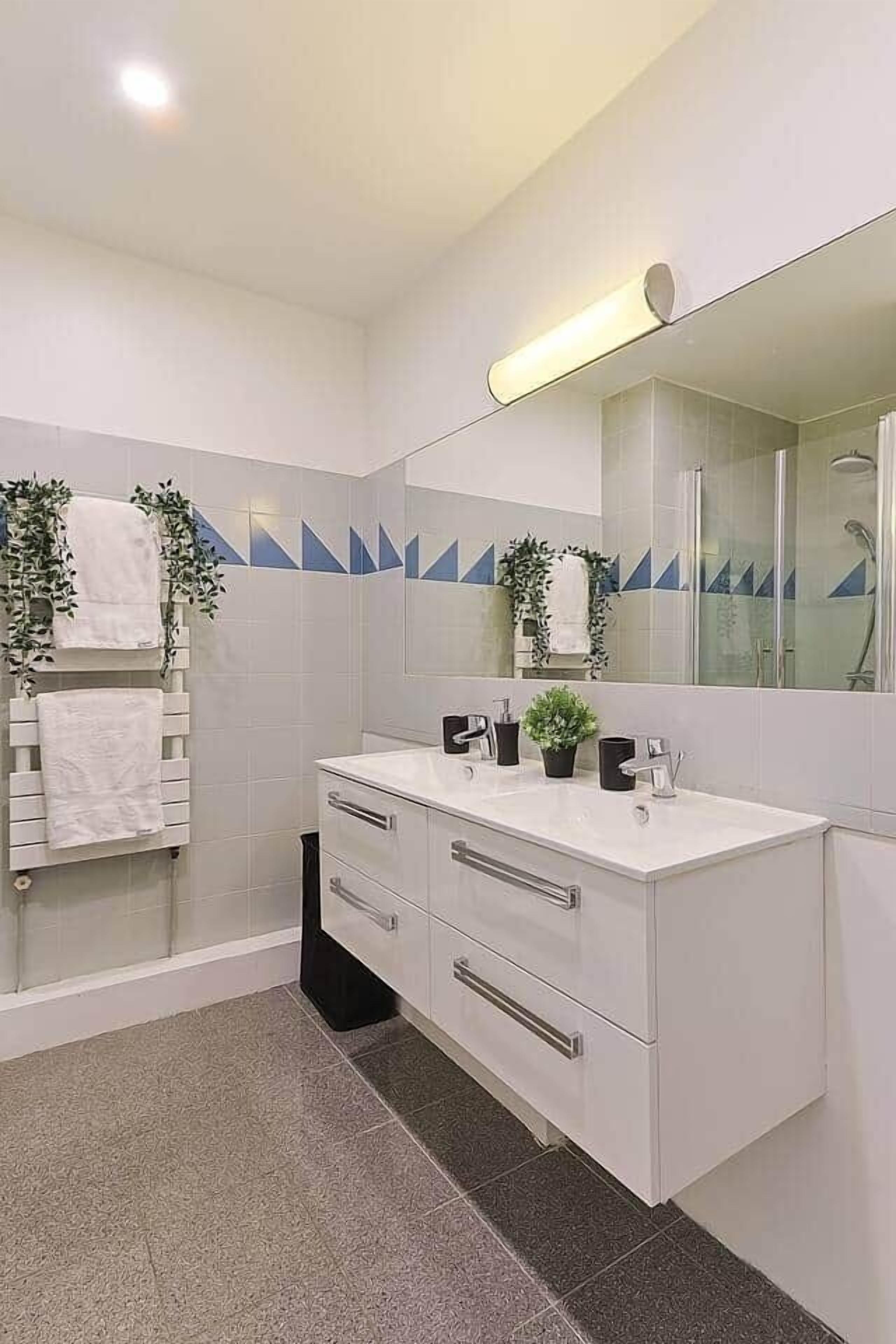 A modern bathroom with a white vanity, a large mirror, and a shower area.