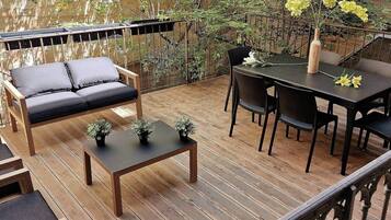 Een houten terras met een bank, tafel, stoelen en een vaas met bloemen.