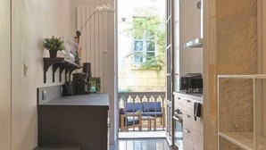 Un corridoio stretto che conduce a un balcone con vista sul verde, una zona cucina con fornelli e pensili, e un cestino.