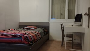 Ett sovrum med en säng, ett skrivbord med en dator och ett fönster.