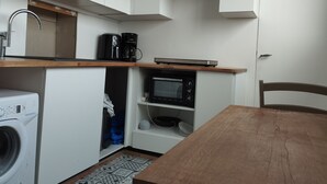 Ett kompakt kök med tvättmaskin, mikrovågsugn och kaffebryggare på bänkskivan.
