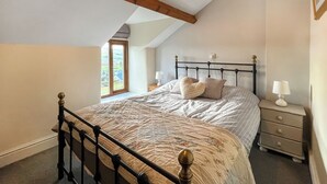 A bedroom with a sloped ceiling, a bed with a quilted cover, two bedside lamps, and a window with a view of greenery. - 2 bedroom accommodation in Betws-Y-Coed (Betws-Y-Coed)
