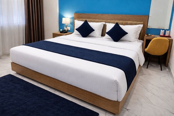 A hotel room with a large bed, a nightstand with a lamp, a chair, and a blue wall.