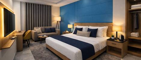 A modern hotel room with a large bed, a desk, a chair, a TV, and a wardrobe.