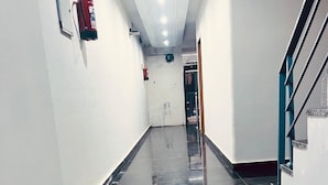 A corridor with a shiny black floor, white walls, and a fire extinguisher mounted on the wall. - Hotel The Rise (New Delhi)