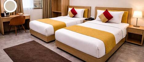 A hotel room with two beds, a desk, a chair, a mirror, and a nightstand.