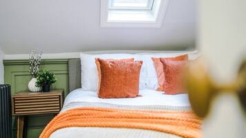A bedroom with a skylight, a bed with white and orange bedding, a bedside table with a plant, and a radiator.