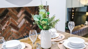 A dining table set with white plates, bowls, cutlery, and wine glasses, with a white vase containing greenery in the center. - Charming 2-bedroom Flat in York - Sleeps 6 (York)