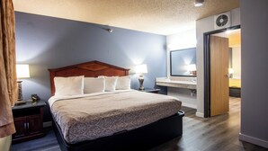Une chambre d’hôtel avec un grand lit, des lampes de chevet, une tête de lit en bois, une table de chevet, un miroir et une porte donnant sur une autre pièce.