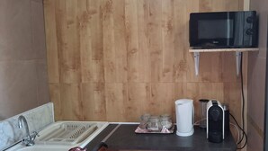 Ett kompakt kök med en mikrovågsugn, vattenkokare och kaffebryggare på en bänkskiva.