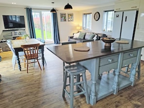 A spacious kitchen with a central island, wooden flooring, and a dining area with chairs and a table. - A charming riverside cottage in Upwell, accommodating up to 7 guests. (Upwell)