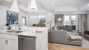 A modern kitchen with a central island, a dining area with a grey sofa, and a large window with curtains. - Elegant Modern Residence! Ritz Carlton Vail. Pool, Hot Tub, Short Walk to Slopes (Vail)