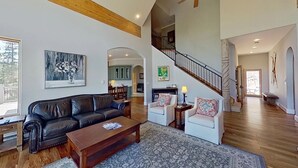 Un salon spacieux, doté d’un canapé en cuir, d’une table basse et d’un tapis à motifs. Un escalier mène à un niveau supérieur où se trouvent une cuisine et un coin repas.