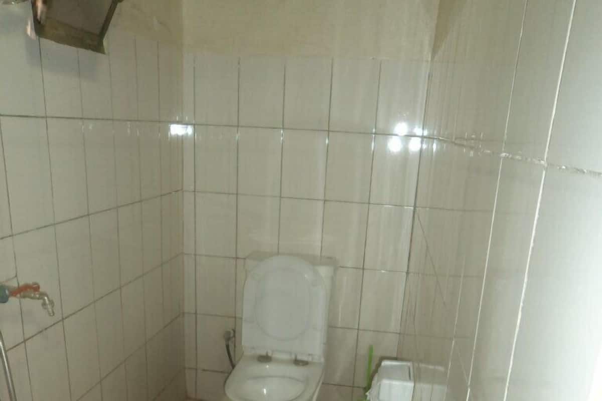 A small, tiled bathroom with a toilet, a hand dryer, and a green cleaning brush.