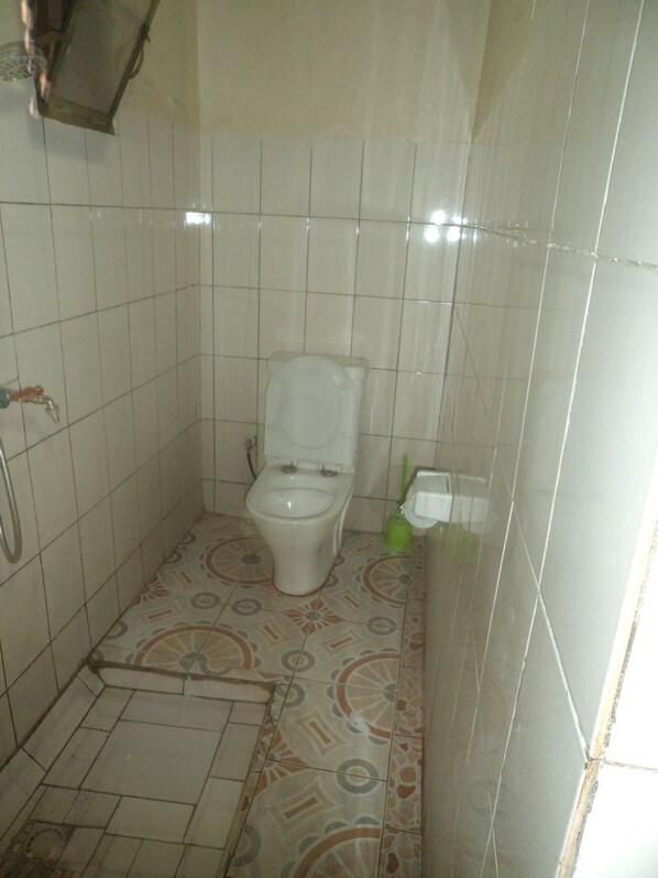 Un baño pequeño con azulejos, un inodoro, un secador de manos y un cepillo de limpieza verde.