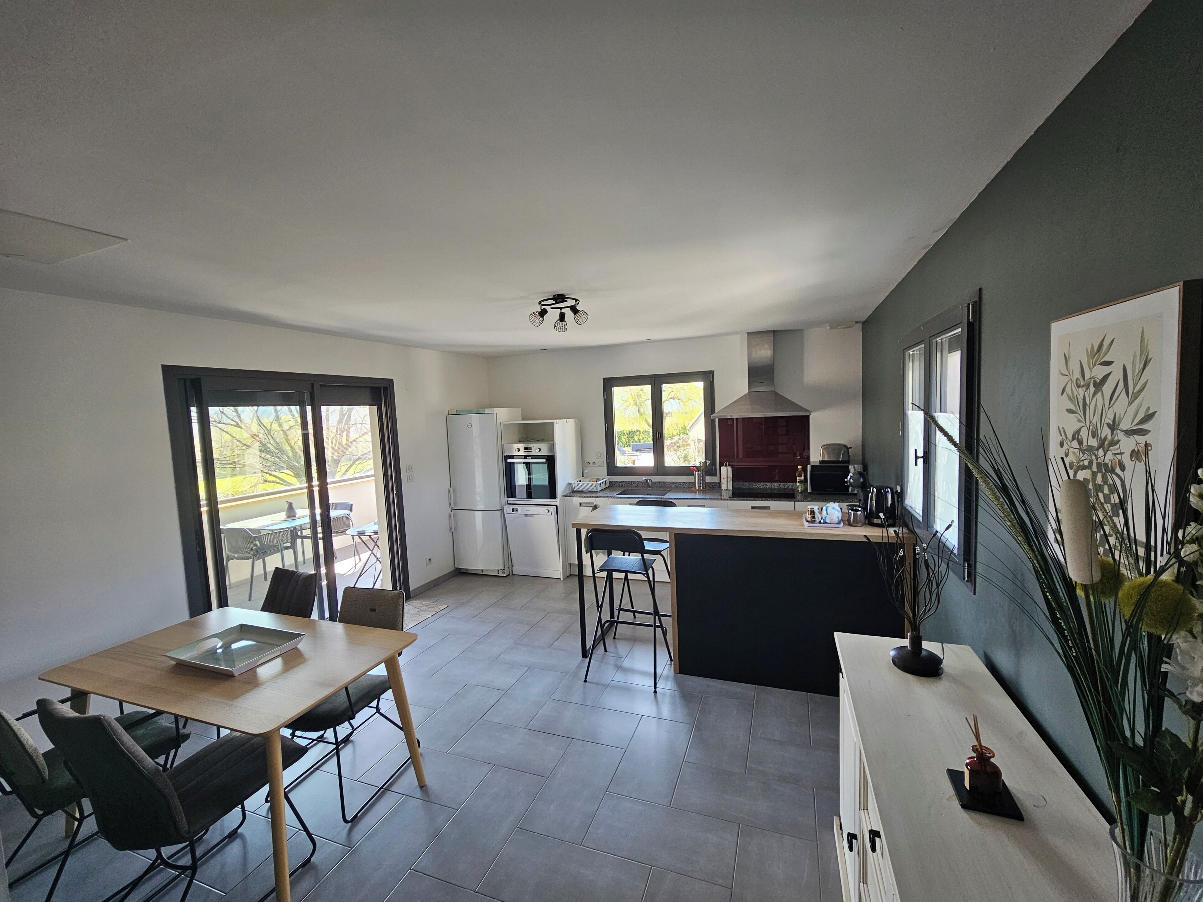 A modern kitchen with a dining area, large windows, and a view of the outdoors.