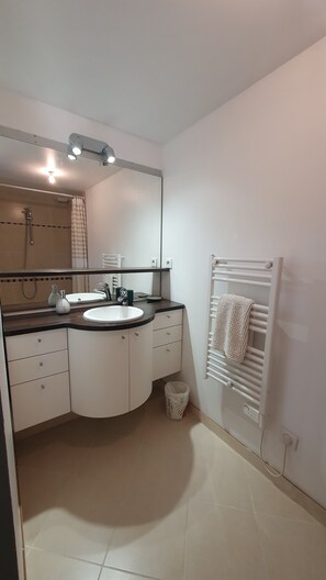 A modern bathroom with a double sink, a mirror, a towel rack, and a shower area.