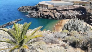Un paysage côtier avec une plage rocheuse, une eau d’un bleu limpide et une végétation clairsemée.