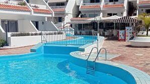 Ein Schwimmbecken mit geschwungener Form, umgeben von einem weißen Gebäude mit roten Ziegeldächern.