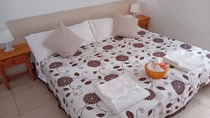 Ein ordentlich bezogenes Bett mit floralem Überwurf, Kissen und einem Korb mit gefalteten Handtüchern.