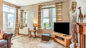 Un salon comprenant un canapé, un téléviseur, une table basse en bois et une cheminée agrémentée d’objets décoratifs.