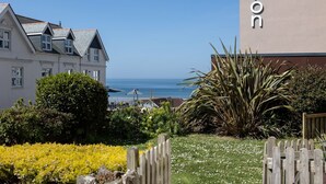 Un hôtel situé sur la côte, avec vue sur la mer, un jardin agrémenté de fleurs jaunes et une clôture en bois.