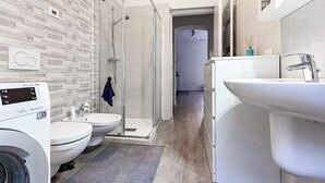 Un baño moderno con lavadora, dos inodoros, ducha y lavamanos.
