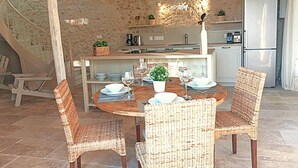Een eethoek met rieten stoelen, een ronde houten tafel en een keuken op de achtergrond.